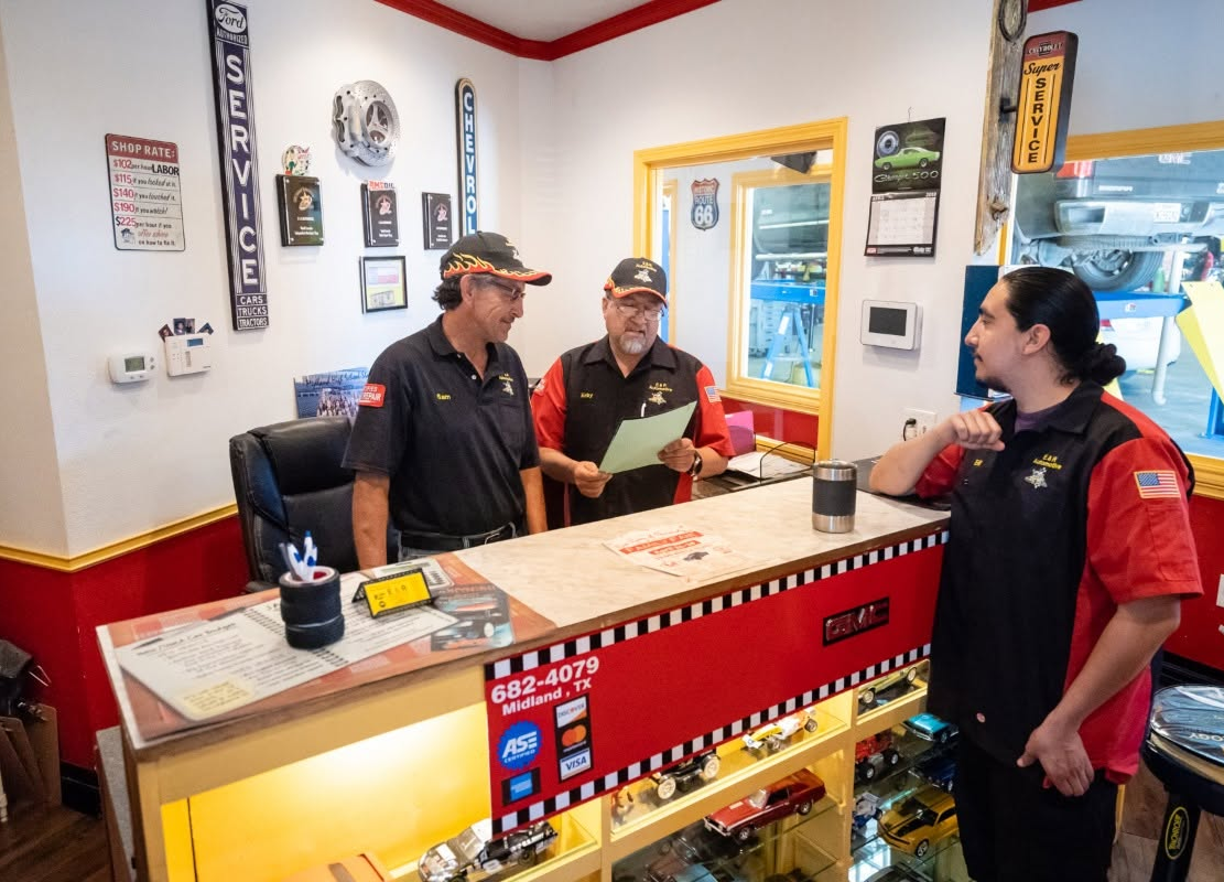 Three employees chatting at a service counter in a bright shop lobby | E&R Automotive