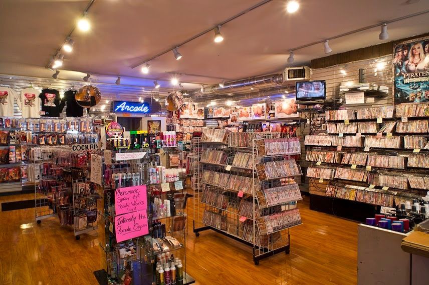 Cluttered gift shop interior with shelves of small items, neon signs, and warm overhead lighting
