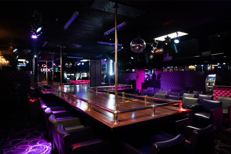Empty nightclub with a central dance floor, bar seating, purple lighting, and a mirrored disco ball.