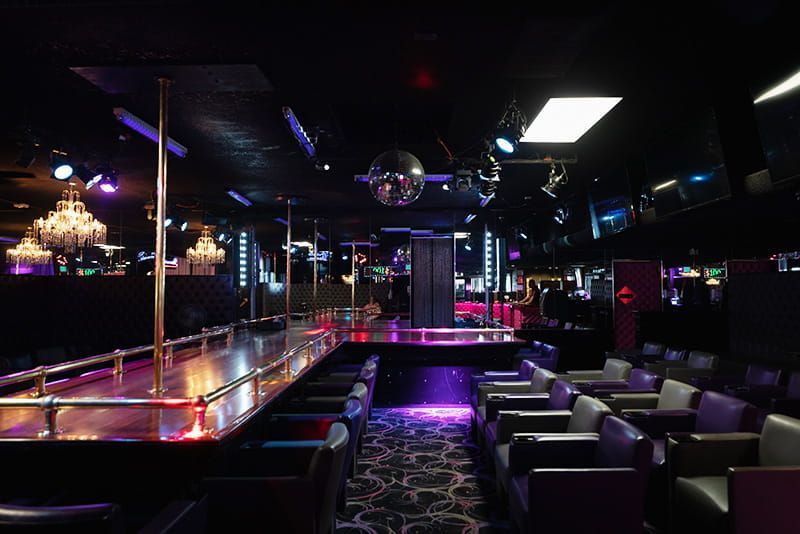 Dim nightclub interior with purple lighting, bar seating, and a central dance floor with disco balls