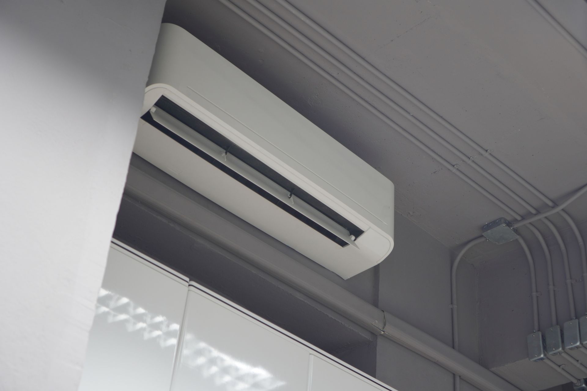 Condizionatore bianco montato su un soffitto grigio. I cavi elettrici corrono lungo la parete.