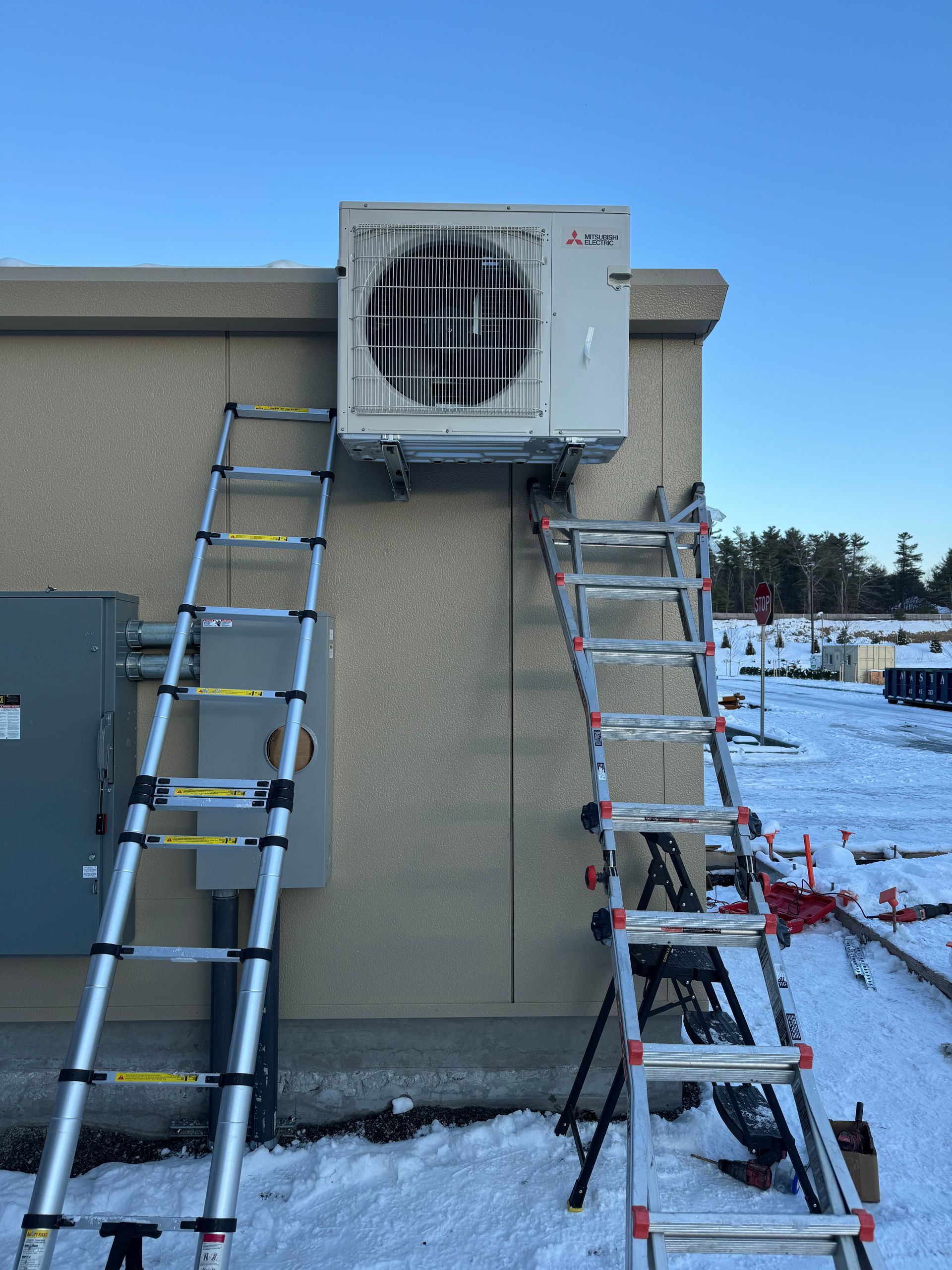 heat pump installation quincy ma Air conditioning unit mounted on a building, two ladders present, snow on the ground.
