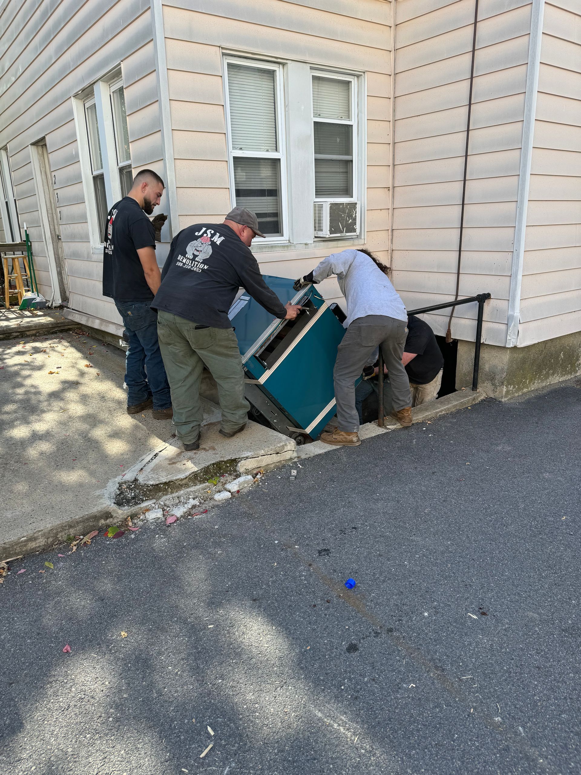 hvac installation quincy ma Four people moving a teal couch into a basement entrance beside a building. Asphalt and grass on the ground.