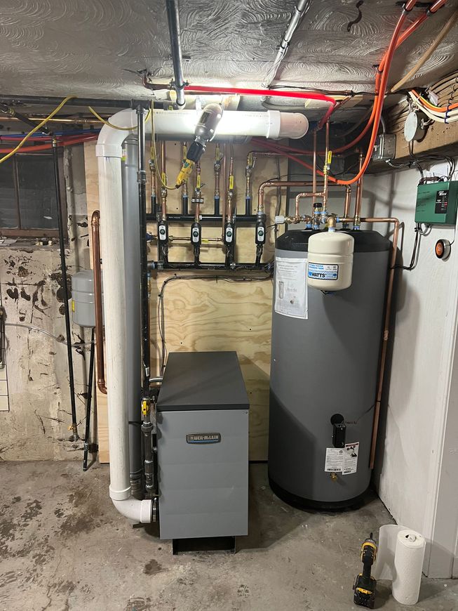 Basement utility room with heating system components: boiler, water heater, pipes, and electrical wiring.