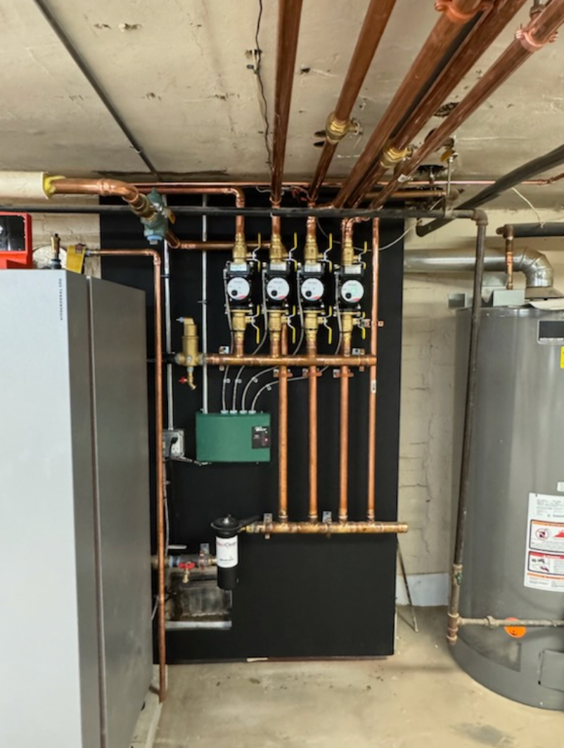 Copper pipes and valves, black panel, and green control box in a utility room.