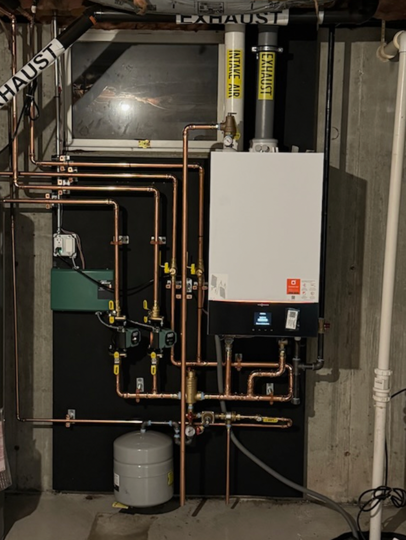 Copper pipe and boiler system in a basement setting, with black insulation, ventilation, and a water tank.