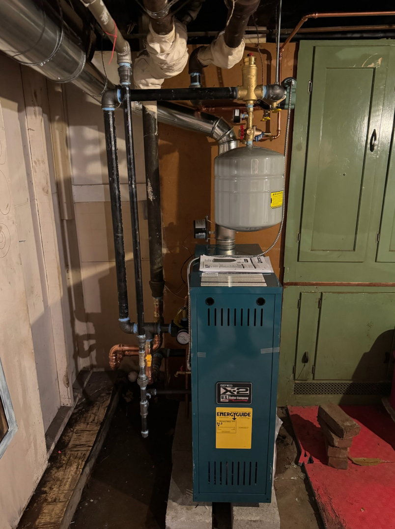 A blue and gray furnace in a basement with connected pipes and tank.