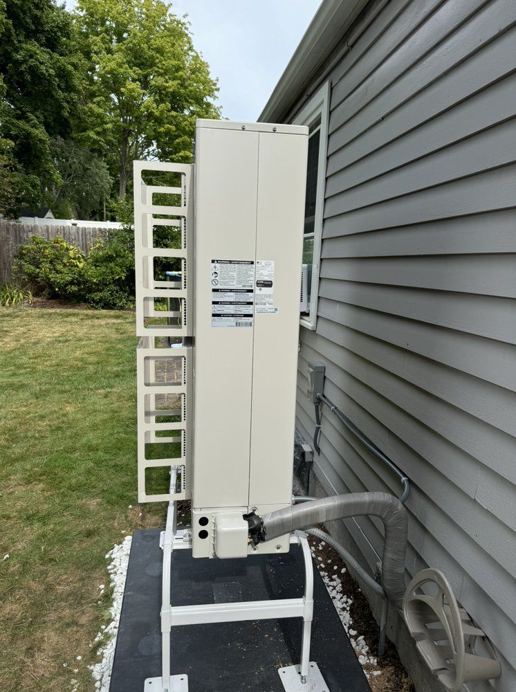 An outdoor HVAC unit attached to a light gray house. Unit is beige, on a white metal stand.