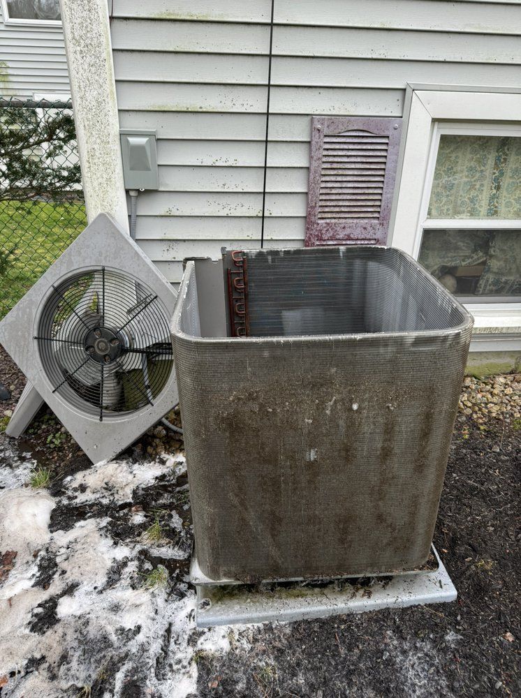 An outdoor air conditioning unit with the fan detached, sitting near a house.