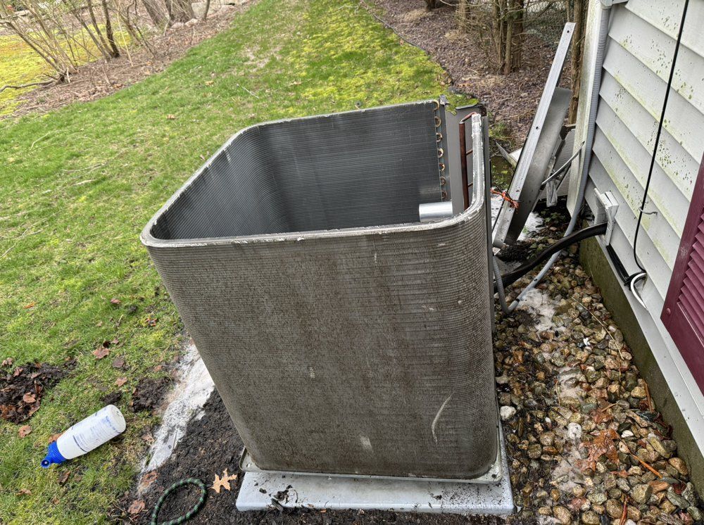 Air conditioning unit with exposed coils, near a house and lawn.