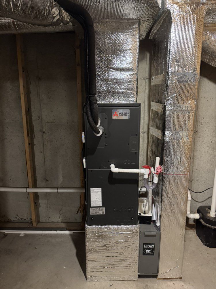 Furnace unit in a basement, with ductwork wrapped in silver insulation.