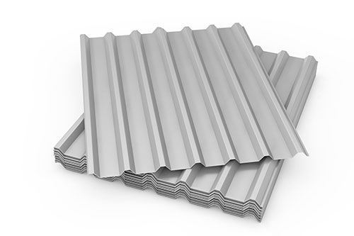 Láminas de metal corrugado plateado apiladas sobre una superficie blanca.