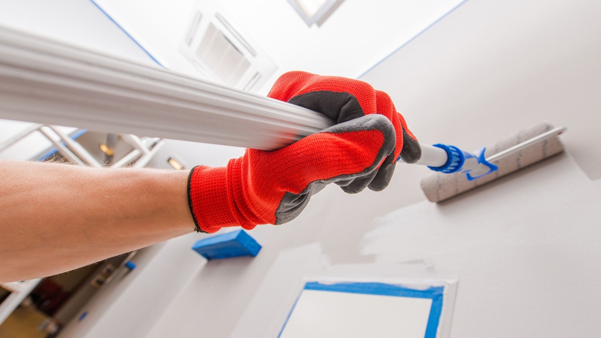 A person wearing red gloves is painting a wall with a paint roller — Allman's Painting in Monkland, QLD