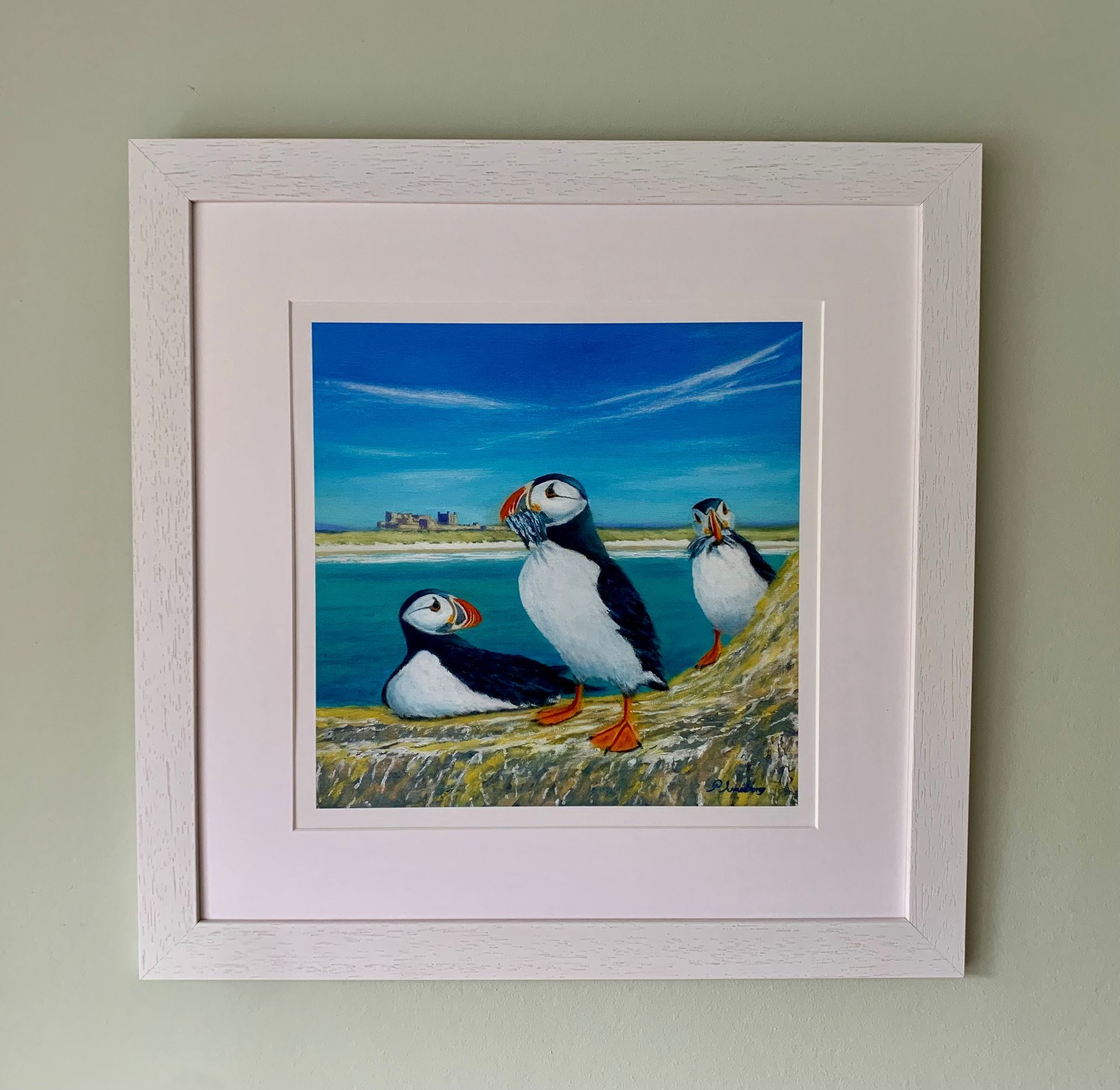 Three puffins on a cliff, ocean and castle in background. One holds fish, all have colorful beaks.