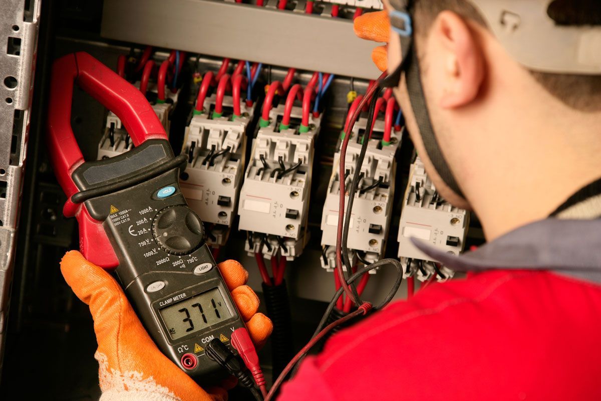 A man is using a clamp meter to check a circuit board.