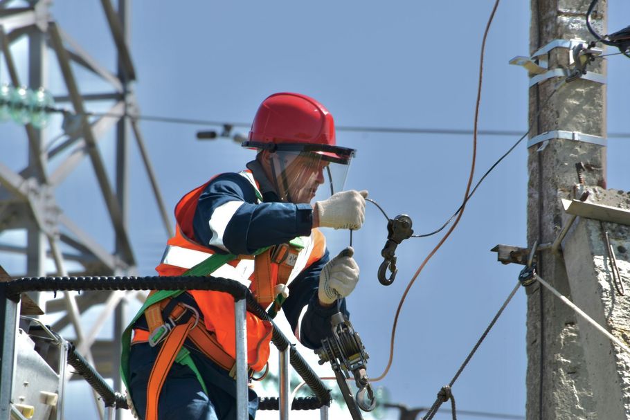 A utility worker in a red hard hat and orange safety vest works on power lines from an aerial lift.