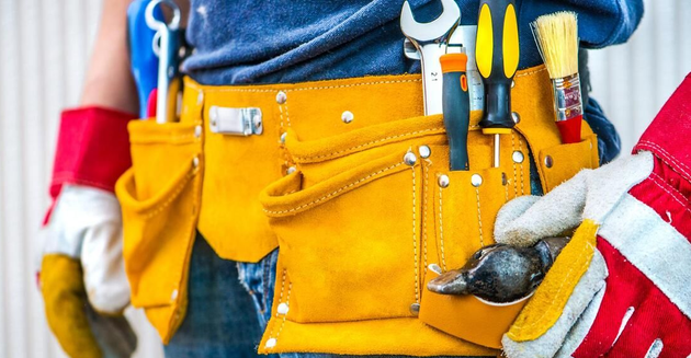 A worker wearing a yellow leather tool belt filled with various tools, gloves, and a hammer.