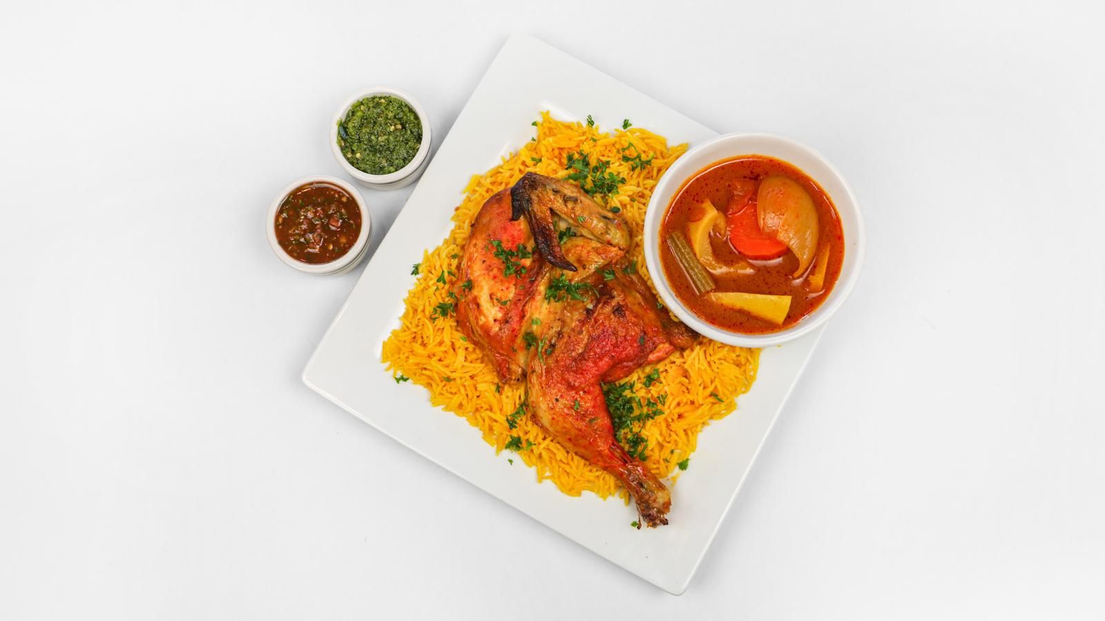 Plate of chicken and yellow rice with a bowl of stew, and small side dishes.