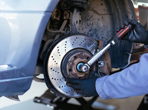 Mechanic loosening a car wheel lug nut with a wrench near a brake rotor