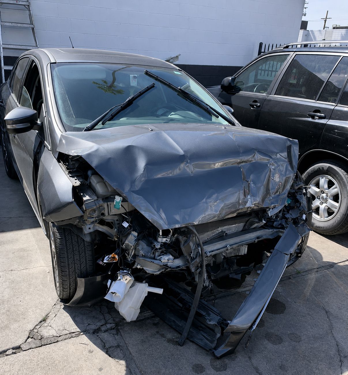 Damaged black car with crushed front end parked beside another vehicle in a lot