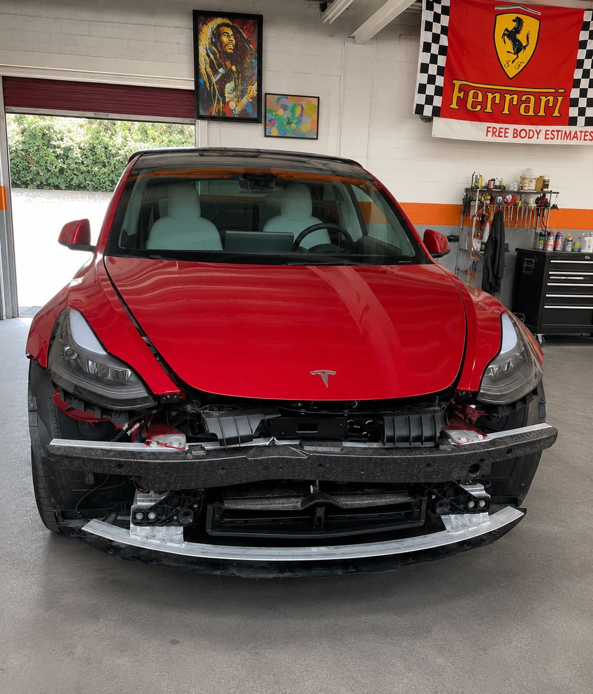 Red Tesla with front-end damage parked in a garage, Ferrari flag on the wall.