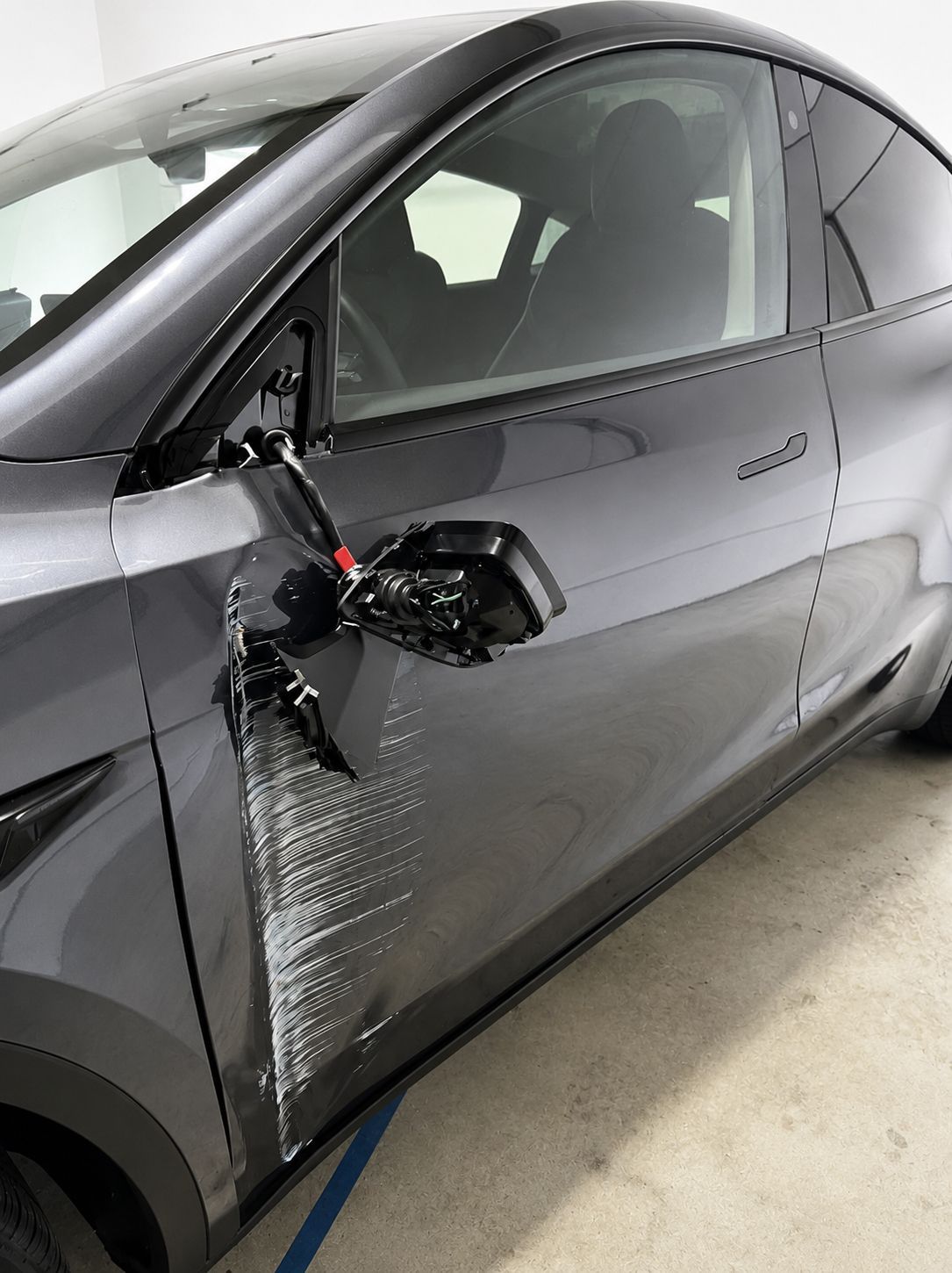 Gray car with damaged driver-side mirror and dented front door in a garage