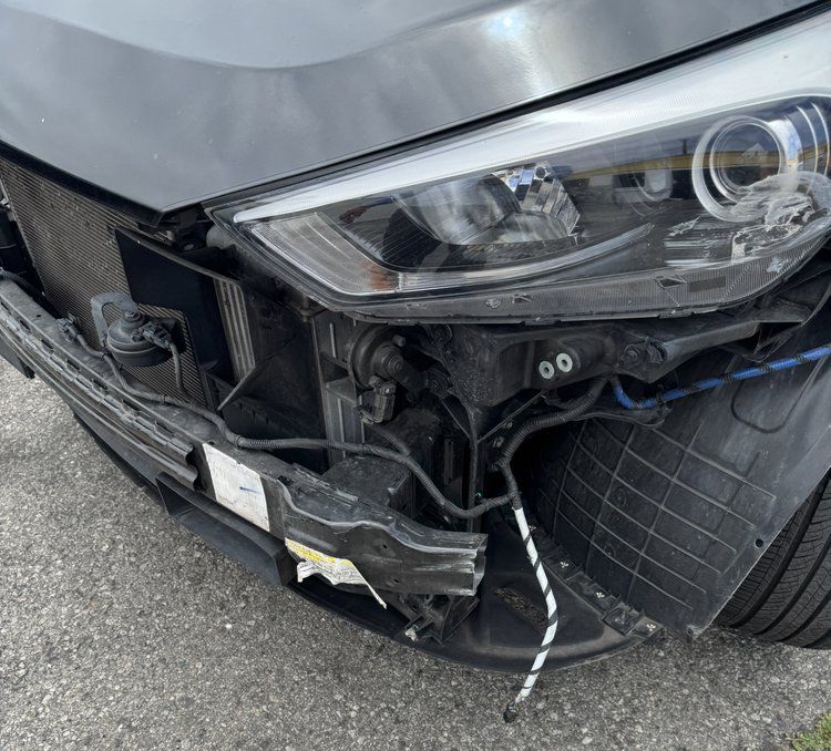 Close-up of a black car’s front-right damage, with broken bumper and exposed headlight area.