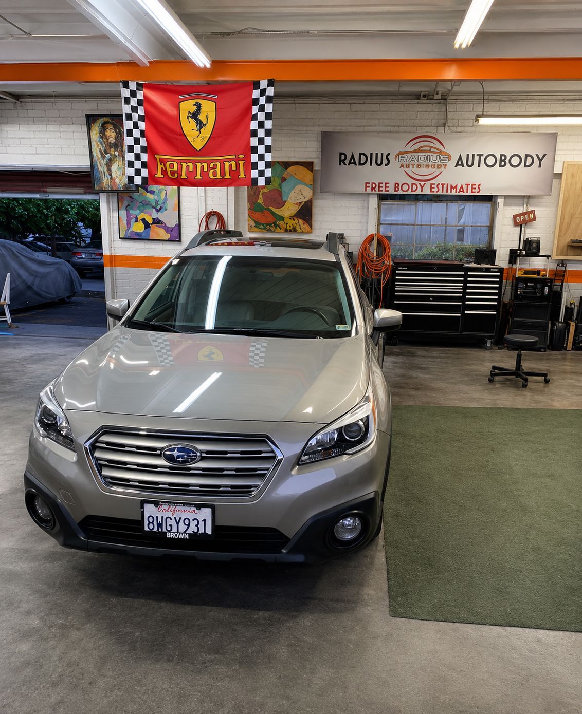 Silver SUV parked inside an auto body shop with banners and tools in the background