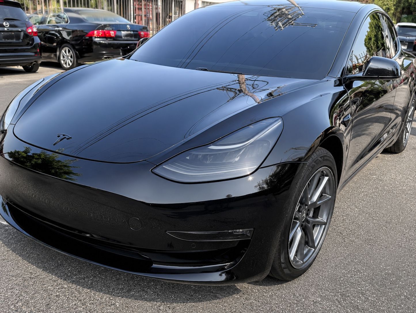 Black Tesla sedan parked outdoors in a lot, front three-quarter view.