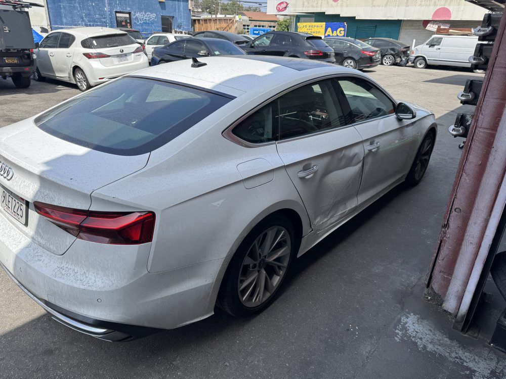 Silver sedan parked beside a building in a parking lot, with other cars in the background.