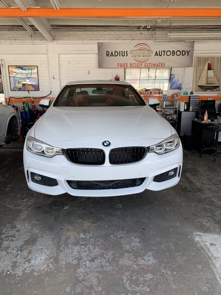 White BMW sedan in an autobody shop garage with tools and equipment around it
