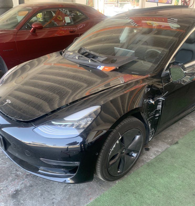 Black Tesla sedan parked indoors beside a red car.
