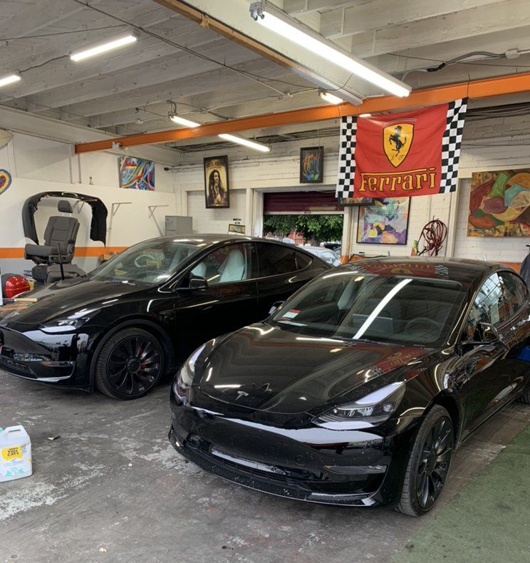 Two black sports cars parked inside a garage with Ferrari decor on the walls
