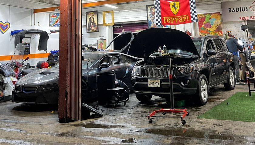 Black SUV in auto repair garage with hood open, surrounded by tools and other cars.