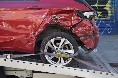 Red car with severe front-right damage on a tow truck bed