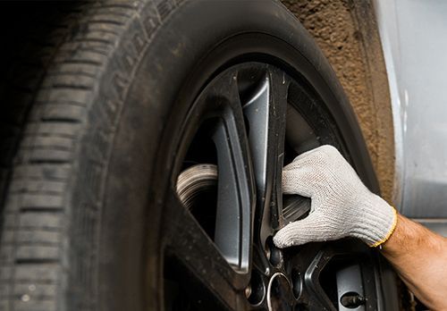 Gloved hand tightening a car wheel lug nut with a wrench, close-up on tire and rim.