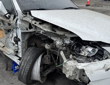Severely damaged silver car after a crash, with crumpled front end and exposed wheel.