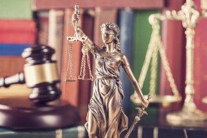 gavel in foreground of a statue of a blindfolded lady holding scales