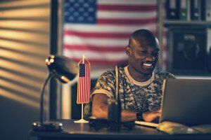 man in camo shirt smiles at laptop