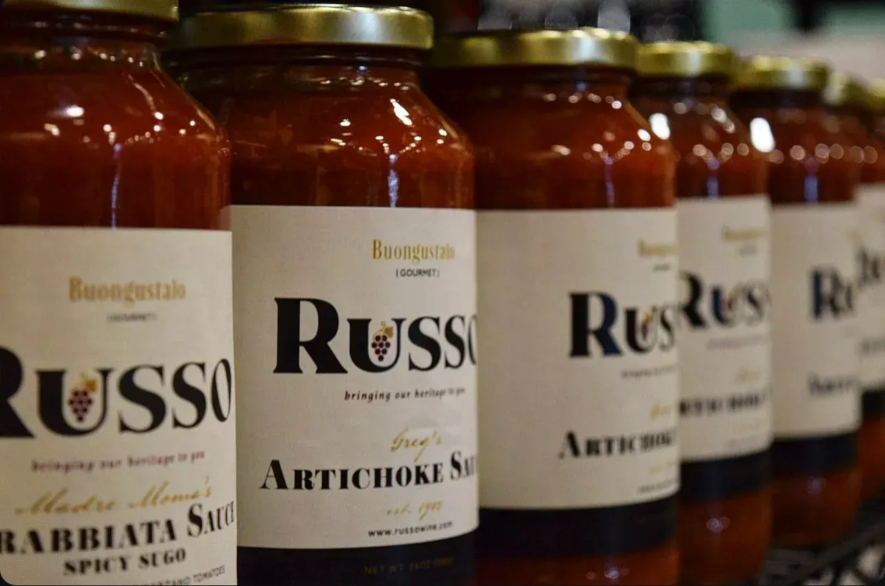 Rows of Russo artichoke sauce jars on a shelf, with white labels and gold lids.