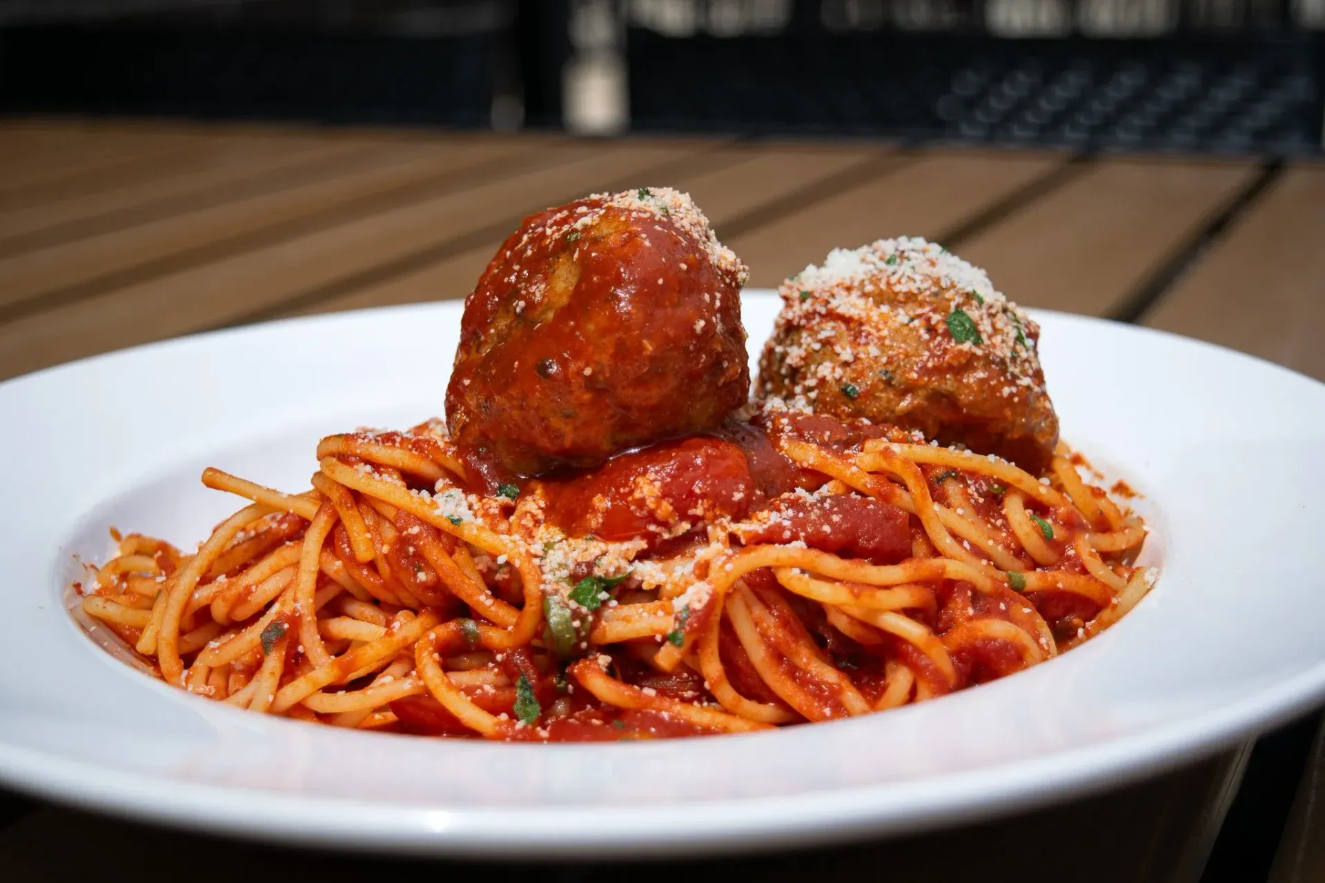 Spaghetti with tomato sauce and two large meatballs, garnished with parmesan, in a white bowl.