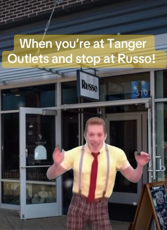 A person in a yellow shirt and red tie gestures excitedly outside of Russo restaurant at Tanger Outlets.