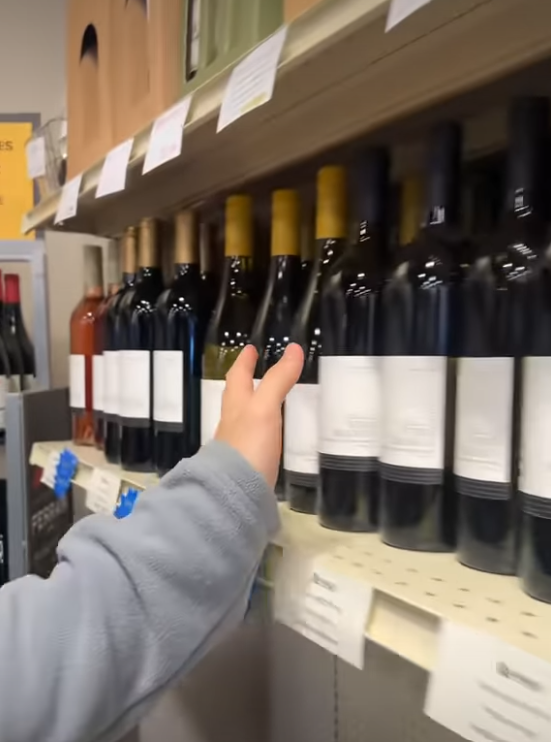 Hand reaching for a wine bottle on a store shelf lined with various bottles.
