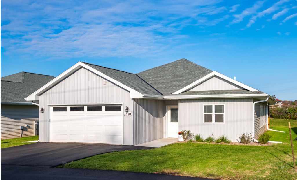 White single-story suburban house with a two-car garage, gray roof, and green lawn under a blue sky
