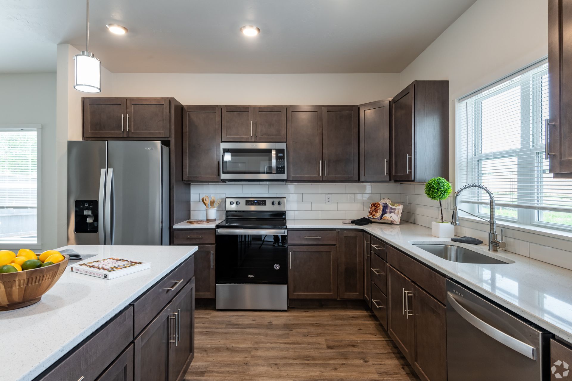 Modern kitchen with dark wood cabinets, stainless appliances, white countertops, and a window over the sink.