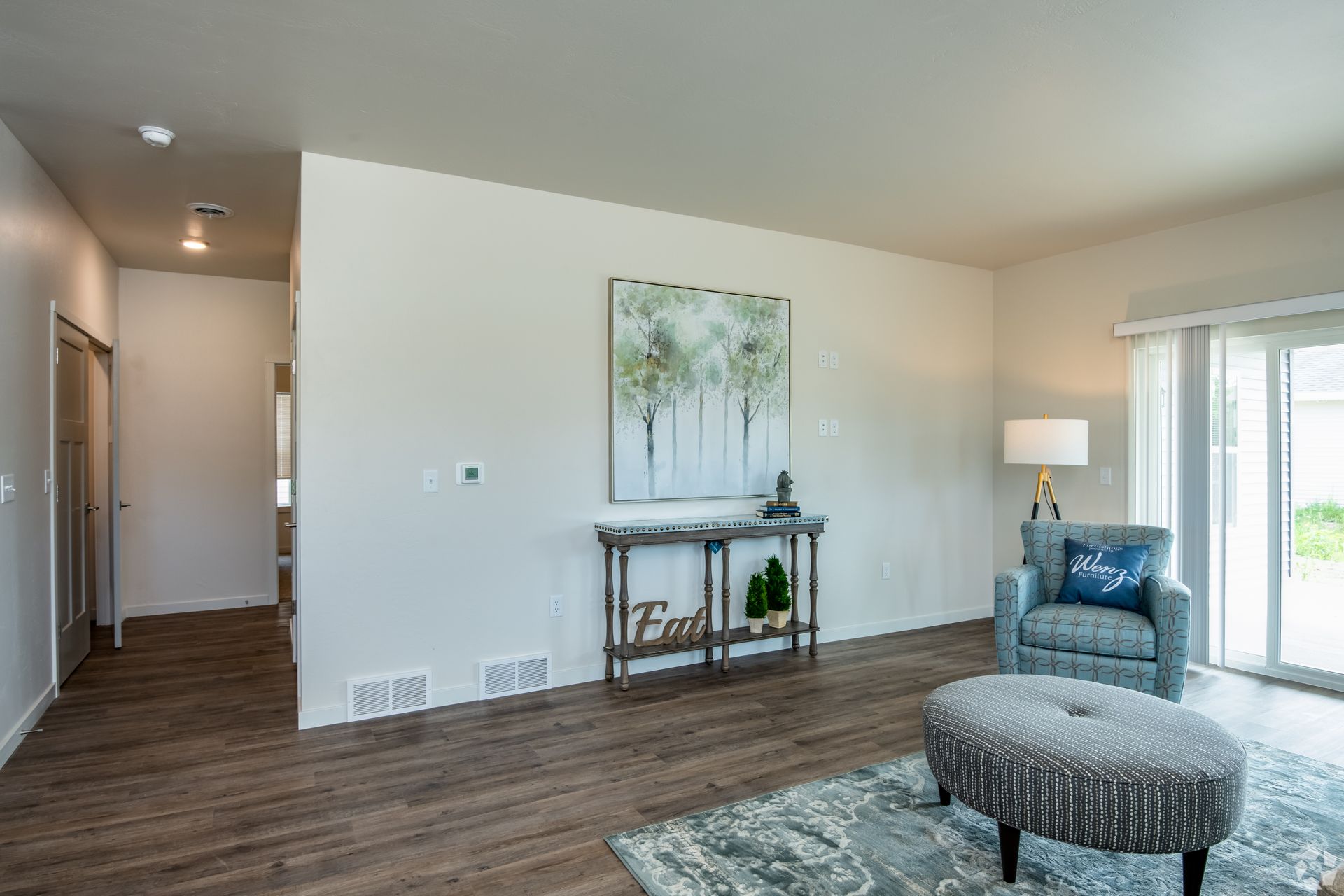 Modern living room with blue chair, ottoman, lamp, and wall art on wood floors