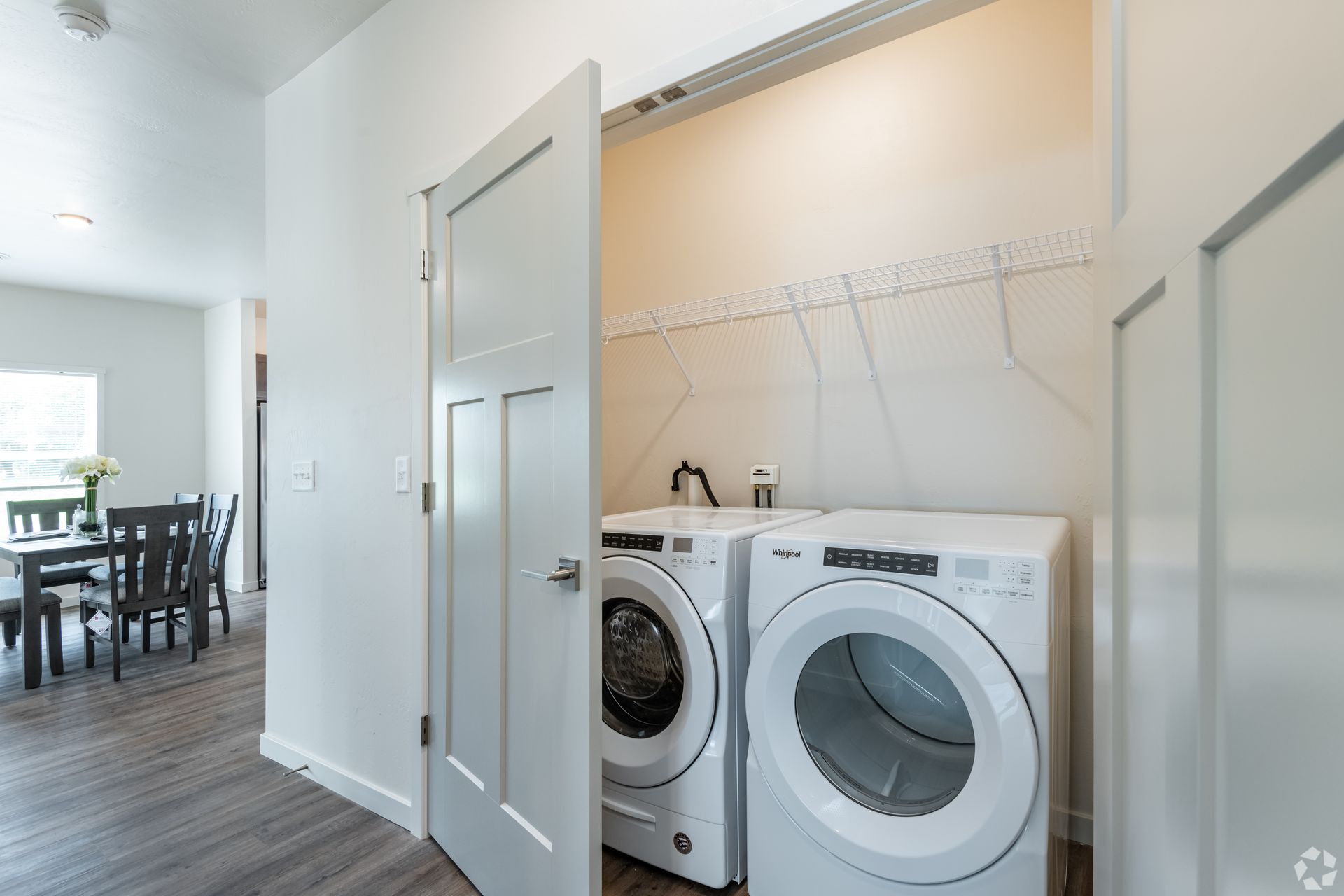 Laundry nook with white washer and dryer in a bright hallway near a dining area