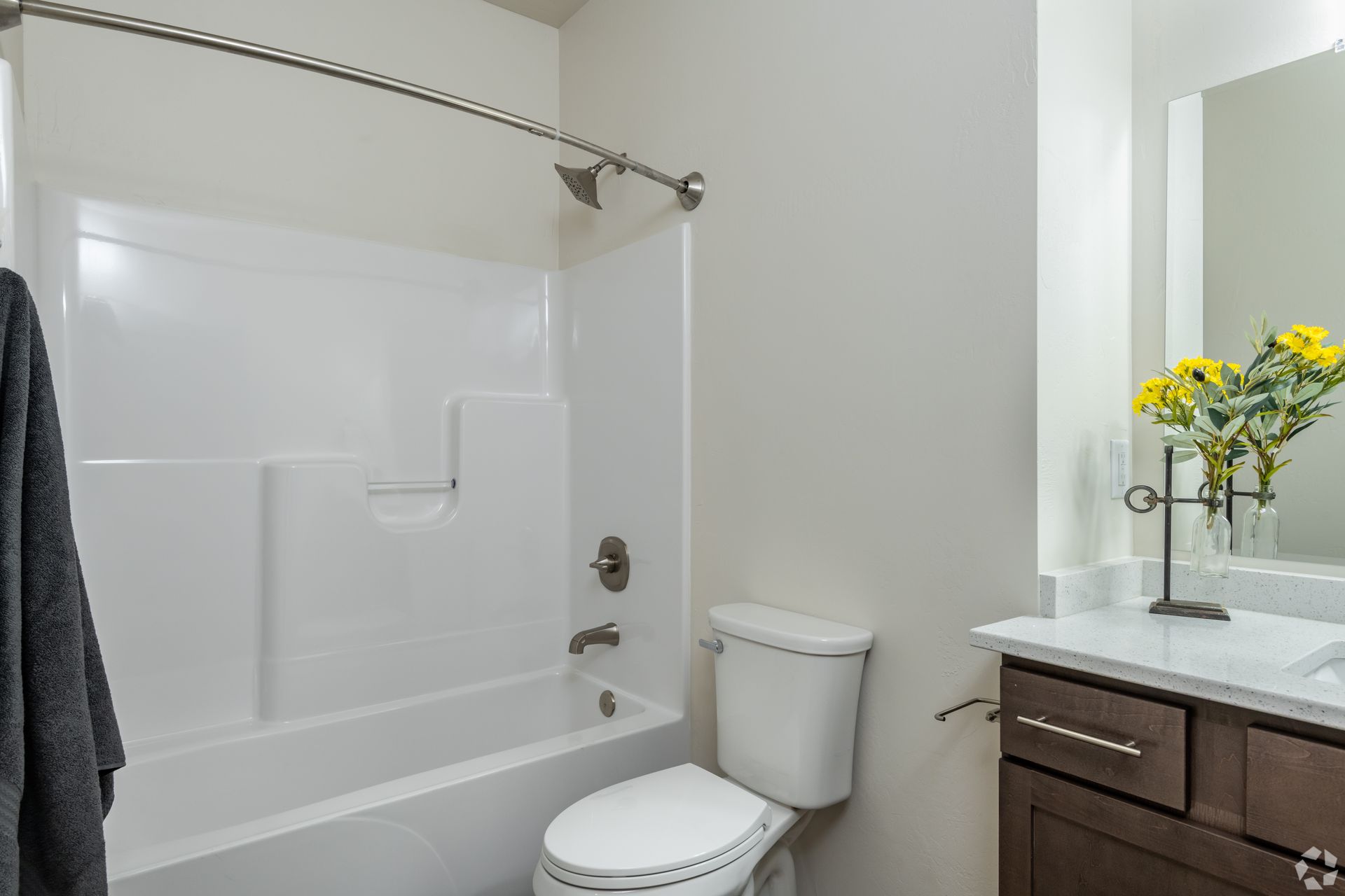 Small bathroom with white tub, toilet, dark vanity, mirror, and yellow flowers on the counter