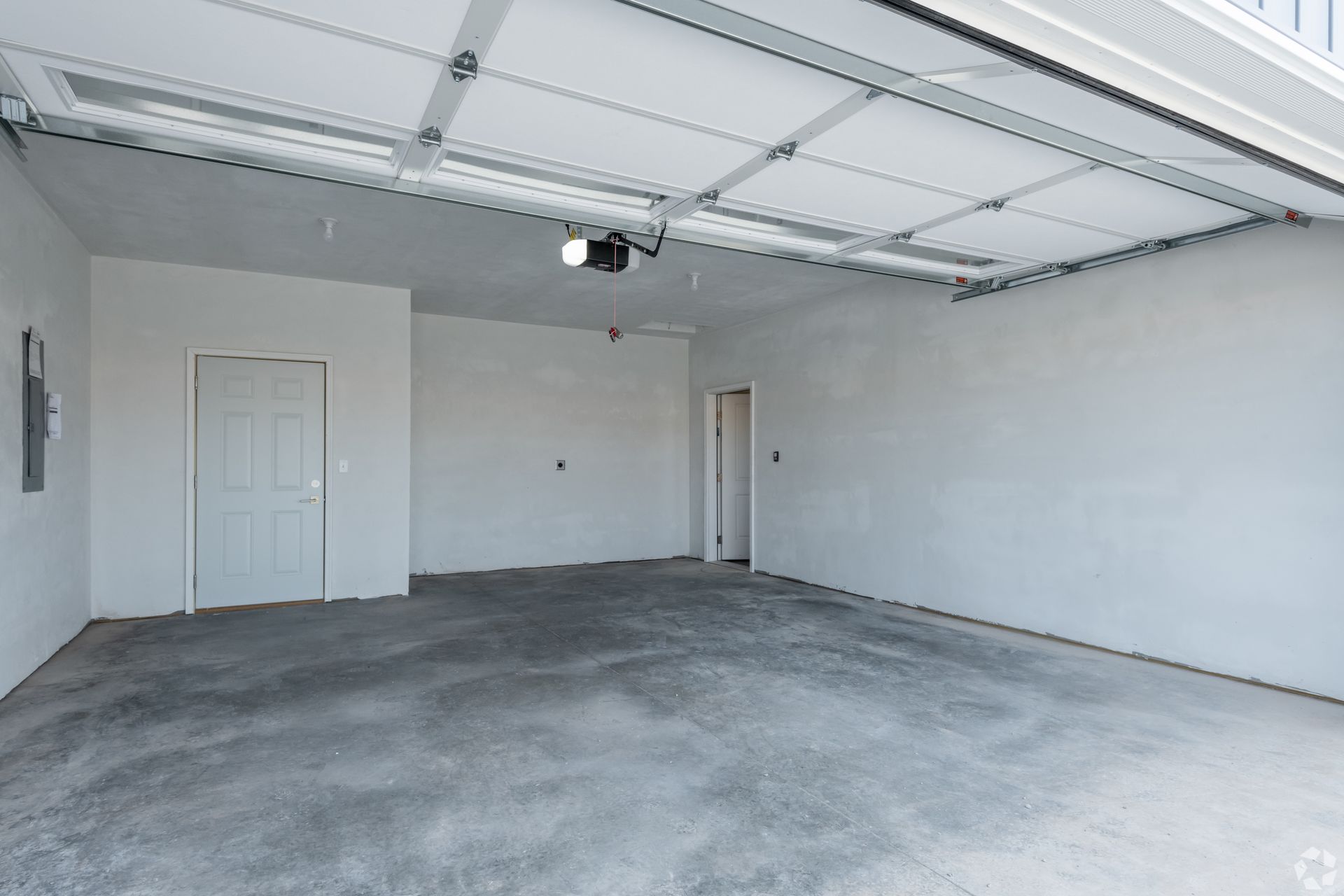 Empty gray garage with concrete floor, white walls, and a closed side door