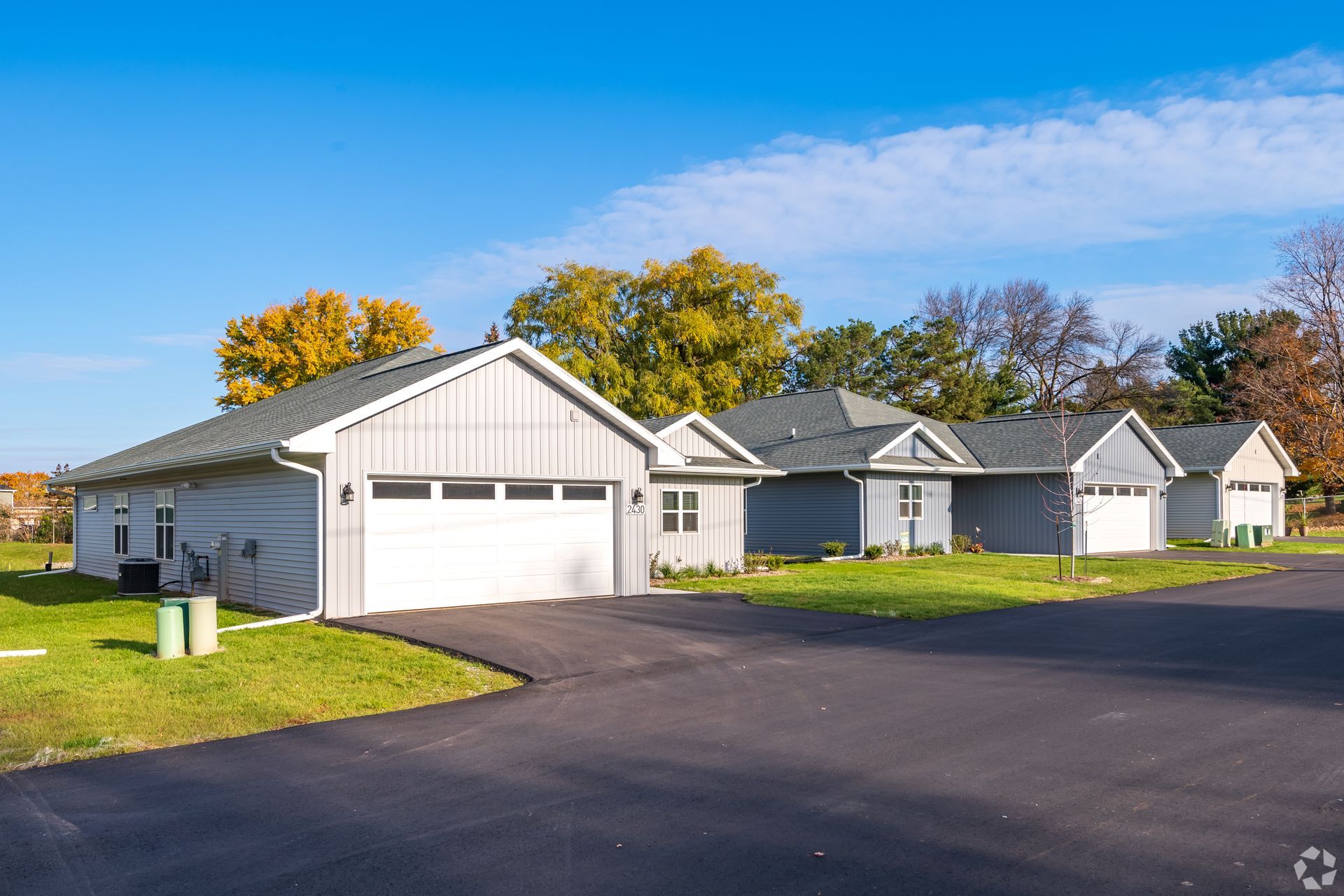 Suburban houses with white garages along a paved driveway under a clear blue sky